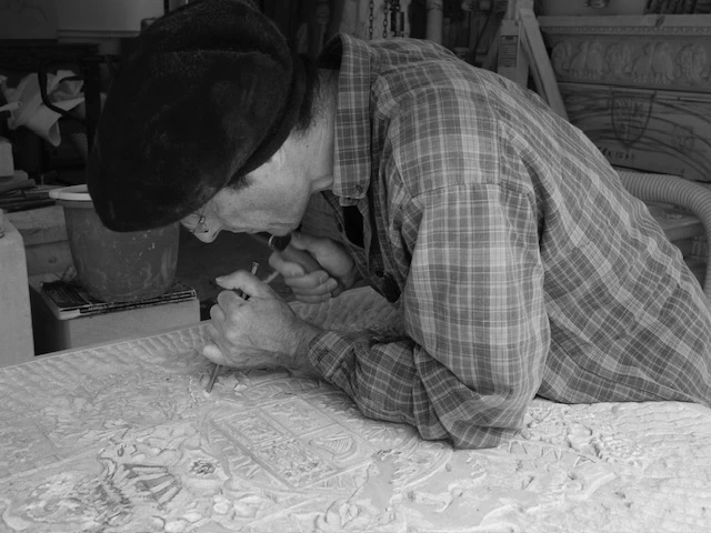 Artisan en train de tailler une pierre avec un marteau et un ciseau dans un atelier de sculpture